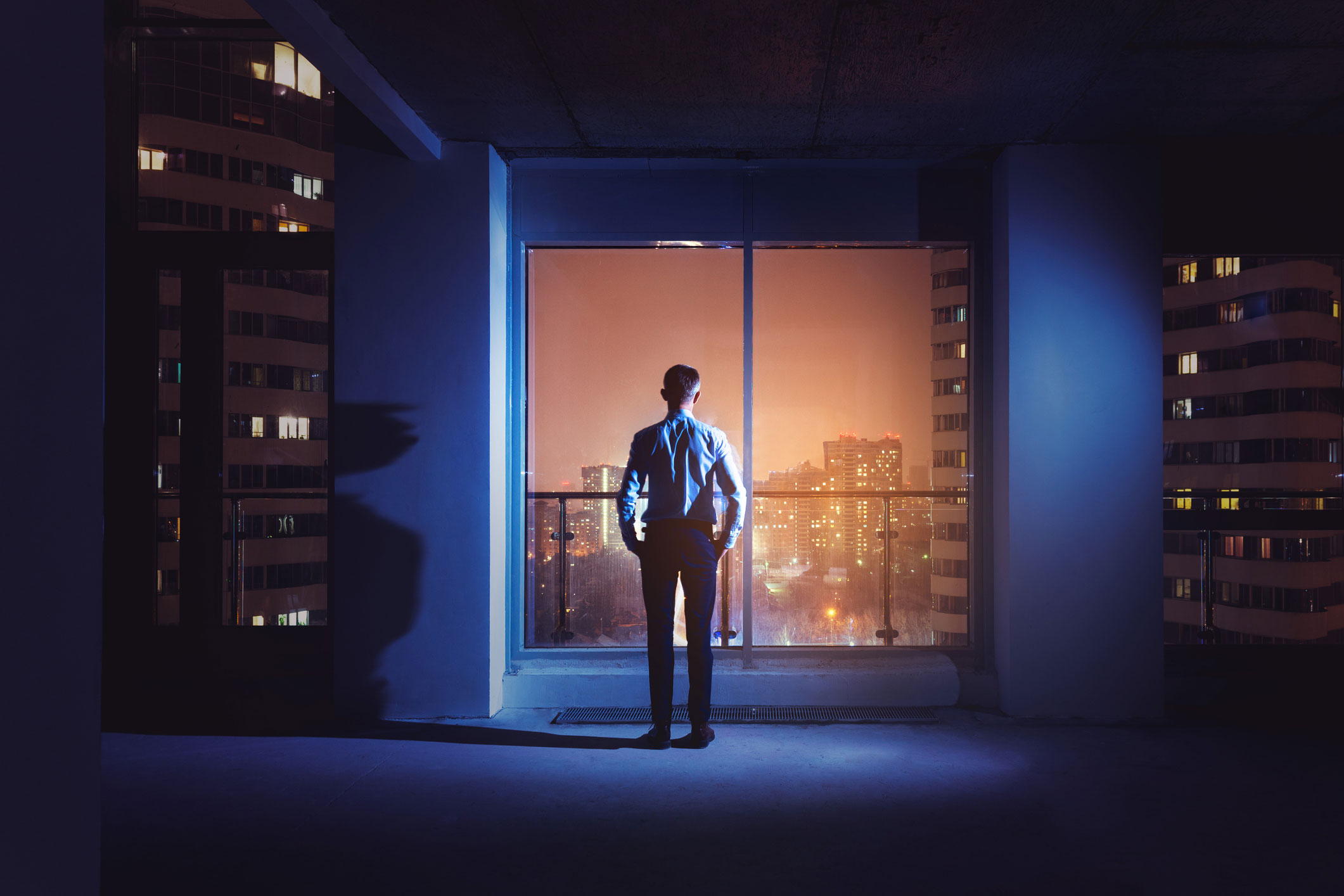 Business man standing looking out a window looking at the city lights at night